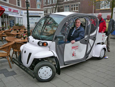 Cafetariahouder Nico Koemans op 4 april bij de opening van zijn pendeldienst in zijn karretje. Henk Bres (geheel rechts) zal kort daarna de eerste rit uitvoeren. Bewoners van zorgcentra en andere slecht ter been zijnden uit de buurt hebben echter nooit gebruik gemaakt van dit gratis vervoer.