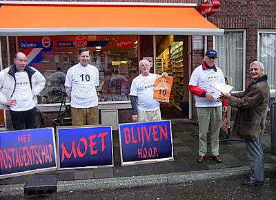 Partijleden Peter Hijmans, Max van der Hoog en Simon Dingemans kijken toe, als René Pasanea, de voorzitter van de wijkvereniging  aan Bert Broeren  de 1500 handtekeningen tegen de geplande sluiting van het postagentschap aan de Mezenlaan overhandigd krijgt.